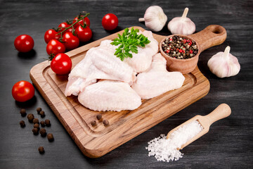 Raw chicken wings with ingredients for cooking on a wooden cutting board on a dark background.