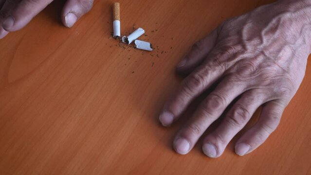 the hands of an old man and a broken cigarette on the table, the harm of tobacco and cigarettes, the fight against addiction to cigarettes. be healthy concept