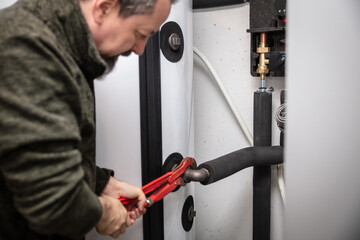 male plumber with pipe wrench installs a new pellet heater in the basement