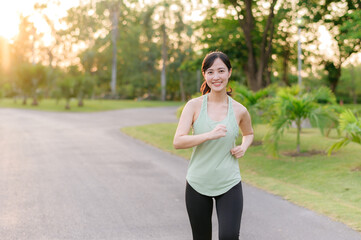 Fit Asian young woman jogging in park smiling happy running and enjoying a healthy outdoor lifestyle. Female jogger. Fitness runner girl in public park. healthy lifestyle and wellness being concept