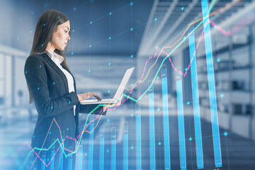 Attractive european businnesswoman using laptop with growing business chart grid on blurry office interior background. Corporate growth plan and company development concept. Double exposure.