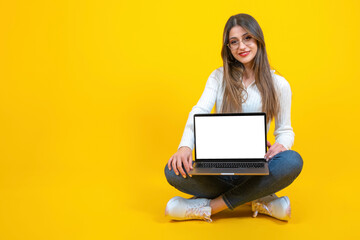 Naklejka premium Modern laptop mockup, real caucasian woman sitting ground holding modern laptop mockup. Smiling positive girl showing notebook with empty blank white screen. Yellow background, copy space. 