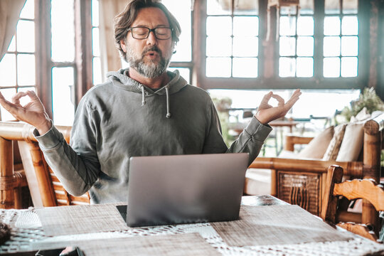 One Serene Adult Man In Relax Position In Front Of A Laptop After Work. Keeping Calm During Smart Working. People Wellbeing At Home Using Computer And Doing Yoga Meditation. Problems And Troubles