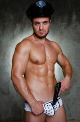Young handsome stripper posing in the studio. A man with an athletic body dressed as a police officer.