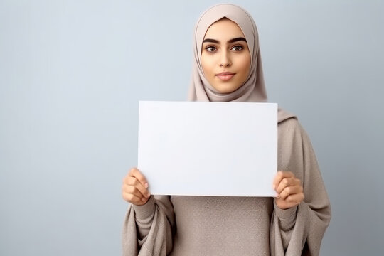 Portrait of beautiful young muslim woman in hijab holding blank sheet of paper on grey background. Generative AI.