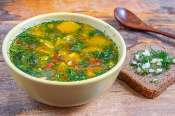 Vegetarian soup with pumpkin and herbs in ceramic bowl over wooden background.