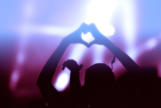 Hands doing the love sign at a concert in front of stage lights