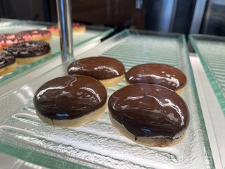 Assorted glazed donuts with chocolate sprinkles topping inside a shop counter