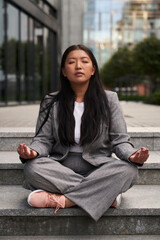 Chinese woman in business outfit meditating out of the building. - obrazy, fototapety, plakaty