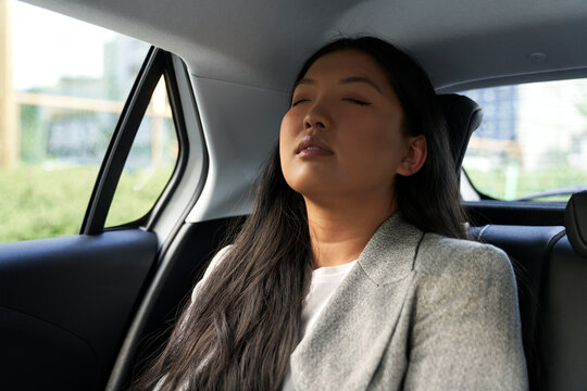 Chinese business woman driving in the car as a passenger with eyes closed