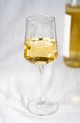 A wineglass of white wine and a bottle in the background in blur. Close-up. Selective focus.