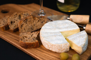 Camembert cheese, fresh crispy baguette on the wooden board on a dark background. Close-up. Selective focus.