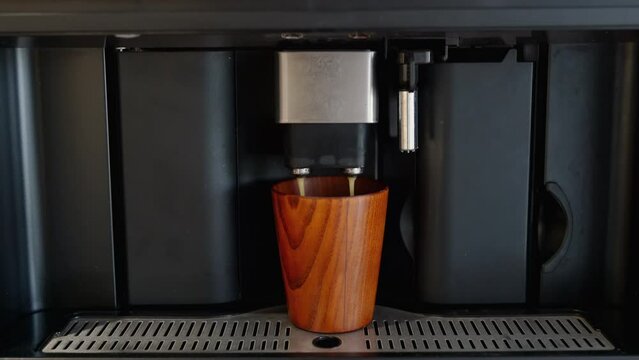 Espresso maker machine pouring black coffee into a wooden glass closeup. Preparation in cup morning capsule coffee with milk or cappuccino close up. Professional home appliances Video footage 4K 25FPS