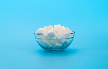 Sugar cubes in a bowl on blue background