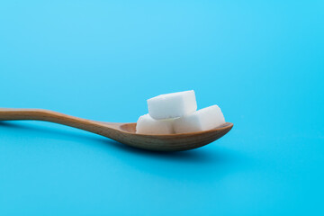 Sugar cubes in wooden spoon on blue background