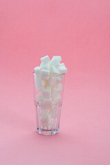 Glass cup full of sugar cubes on pink background