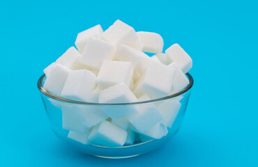 Sugar cubes in a bowl on blue background