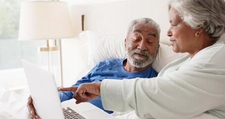 Happy senior biracial couple lying on bed and using laptop, unaltered, in slow motion - Powered by Adobe