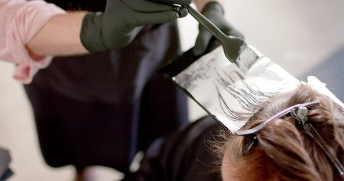 Caucasian male hairdresser highlighting client's hair with brush and foil at salon, in slow motion