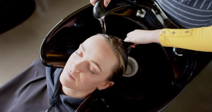 Hands of caucasian female hairdresser washing hair of relaxed female customer at hair salon