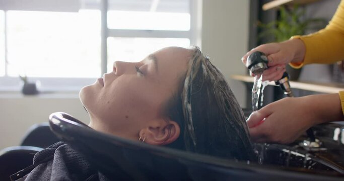 Hands of caucasian female hairdresser washing hair of relaxed female customer at hair salon