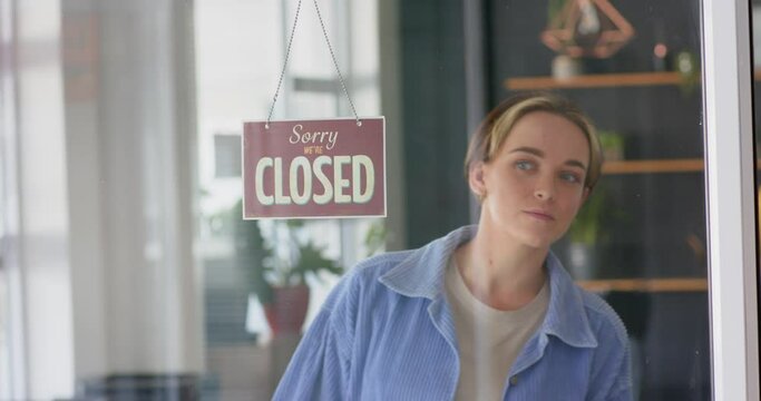 Smiling caucasian female hairdresser turning shop sign to open on door of hair salon, in slow motion