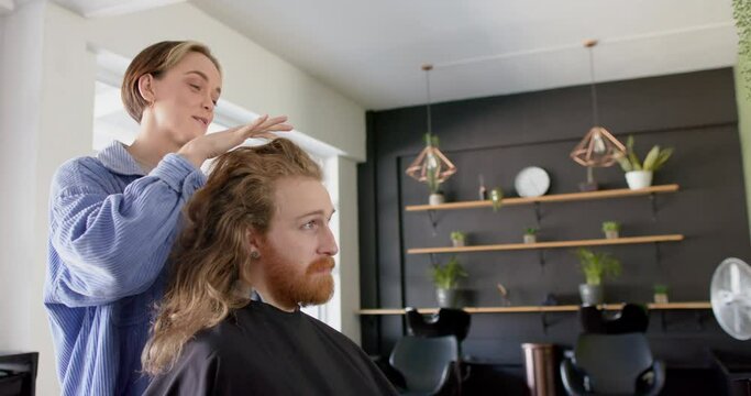 Happy caucasian female hairdresser advising male client with long hair at salon, in slow motion