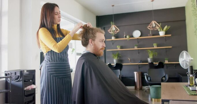 Caucasian female hairdresser untying long hair of male client at hair salon, in slow motion
