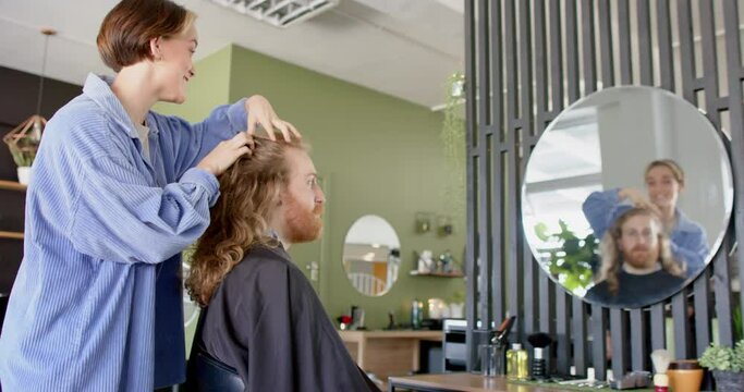 Happy caucasian female hairdresser advising male client with long hair at salon, in slow motion