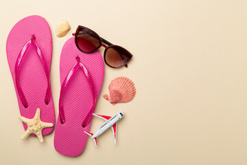 Flip flops with sunglasses and airplane on color background, top view
