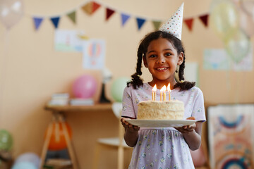 Waist up portrait of black little girl holding birthday cake with candles and smiling at camera, copy space