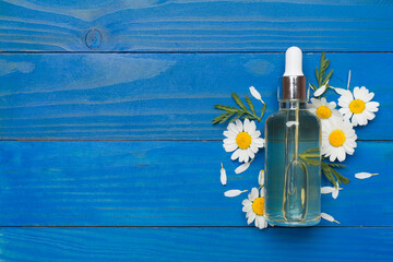 Bottle with chamomile essential oil and flowers on wooden background, top view