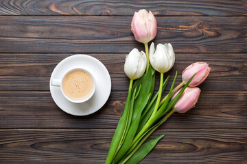 Spring background with flowers, a cup of coffee and a bouquet of pink and white tulips on colored table background with place for text. Copy space top view