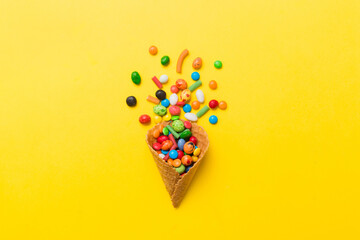 waffle cone full of assorted traditional candies falling out on colored background with copy space....