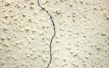 Crack on a beige, yellow plaster wall. Cracked plaster. Damaged wall.