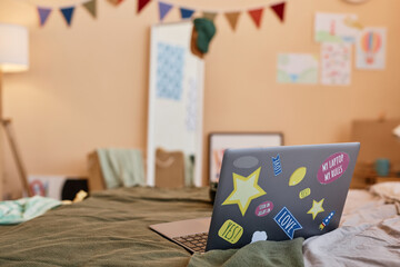 Closeup of laptop decorated with stickers on bed in teenagers room, copy space