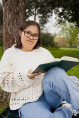 Obraz premium Curvy woman with Down syndrome reading in the park