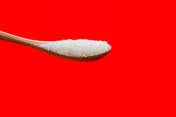 Wooden spoon with sugar crystals on red background