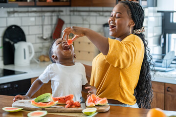 Cheerful African-American mother and son eating a tasty watermelon at home. Flavors of summer