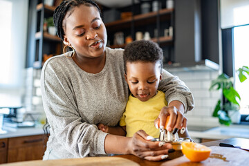 Cheerful African-American mother and son in the kitchen preparing a healthy fruit snack and orange juice