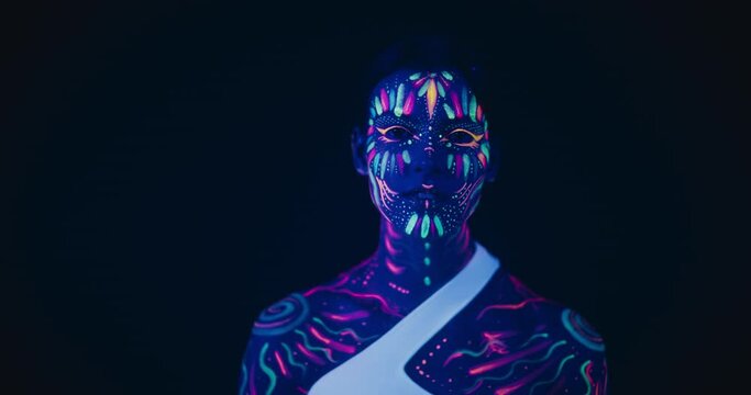 Expressive Portrait: Beautiful Young Woman with Neon Body Paint Looking at Camera, Transmitting a Sense of Alien Nature and Captivation Through Her Intense Gaze and Striking Appearance in a Dark Space