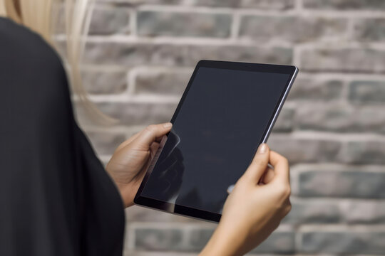 Mockup image of female hands holding and using black tablet pc with blank black desktop screen. Generative AI