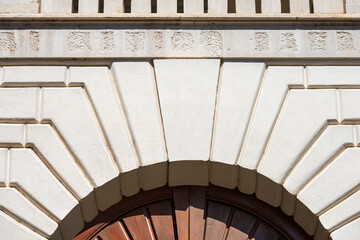 Closeup of a medieval white marble arch with keystone and brown wooden door, full frame, photography. Brescia downtown, Lombardy, Italy, Europe.