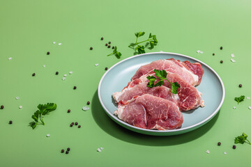 Pieces of pork meat with parsley on gray dish, raw fresh steaks concept. Sea salt, spices
