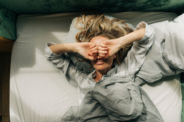A woman wakes up, stretches, rubbing her eyes, lying in bed.
