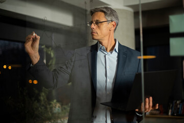 Portrait of successful businessman in office. Man writing on the glass board in office