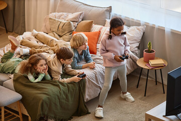 High angle view at group of children playing videogames together and lying on bed, copy space