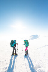 two girls look at the mountains during a winter hike. Two young girls in snowshoes and with backpacks stand on a pass in the mountains.