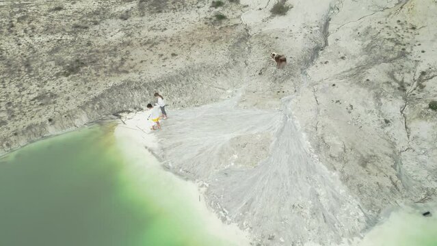 Two children and a dog discover the beauty of a kaolin quarry and a turquoise lake. Top down shot.