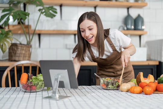 Image of young pretty lady in kitchen and cooking the salad. Looking at tablet computer